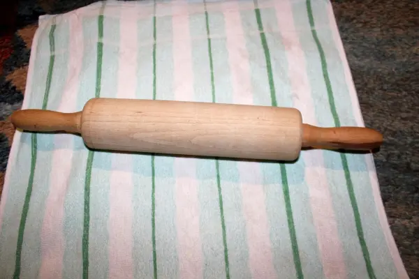 Ein Holztaisenroller liegt auf einem gestreiften Küchentuch, bereit zum Ausrollen von Teig gegen Mandelentzündung und Halsschmerzen.