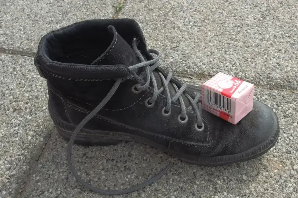 Ein schwarzer Schuh steht auf dem Boden, während ein Päckchen Hefe oben darauf platziert ist, um Fußpilz zu behandeln.