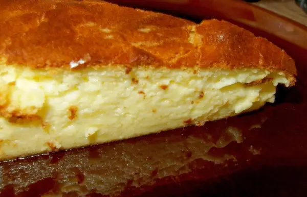Ein Käsekuchen ohne Boden liegt auf einem Teller und zeigt eine goldbraune, leicht gebräunte Oberfläche, umgeben von einem schlichten Hintergrund.
