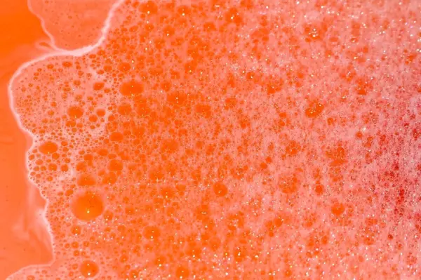 Oranges, schäumendes Badewasser sprudelt, bedeckt mit vielen kleinen Blasen, und füllt einen bunten Badebereich aus.