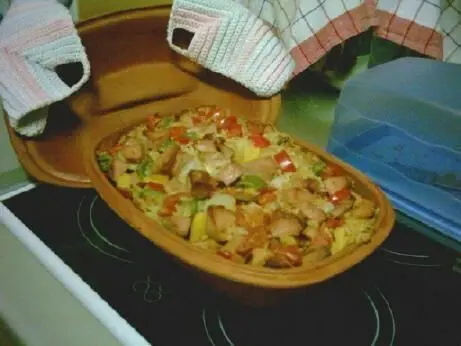 Ein Römertopf mit serbischem Reisfleisch und buntem Gemüse steht auf dem Herd, bereit zum Servieren.
