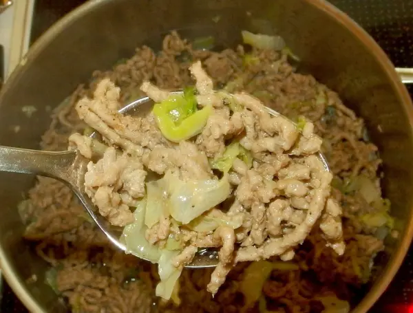 Ein Löffel mit gehacktem Fleisch und Chinakohl wird aus einem Topf mit Eintopf genommen, um serviert zu werden.