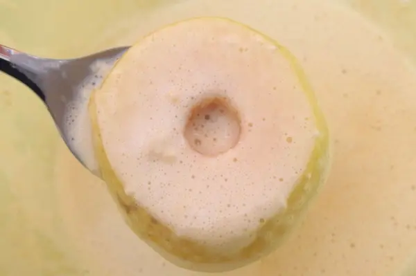 Ein Apfel wird mit einer Gabel aus einem Teig herausgehoben, um für Omas Apfelküchle vorbereitet zu werden.