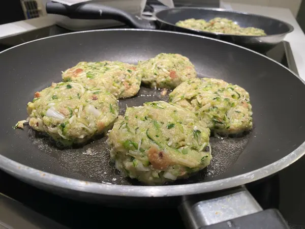 Zucchinipuffer braten in einer Pfanne, umgeben von Küche, während sie goldbraun und knusprig werden.