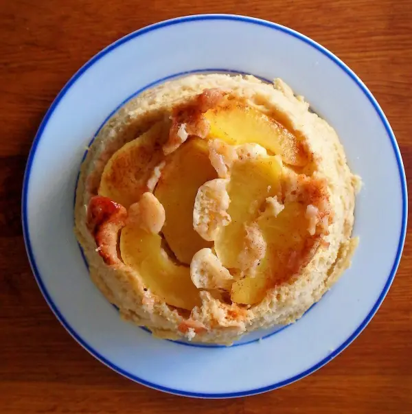 Apfelkuchen liegt appetitlich auf einem blauen Teller, holziger Tisch im Hintergrund. Keine Textbeschriftungen vorhanden.