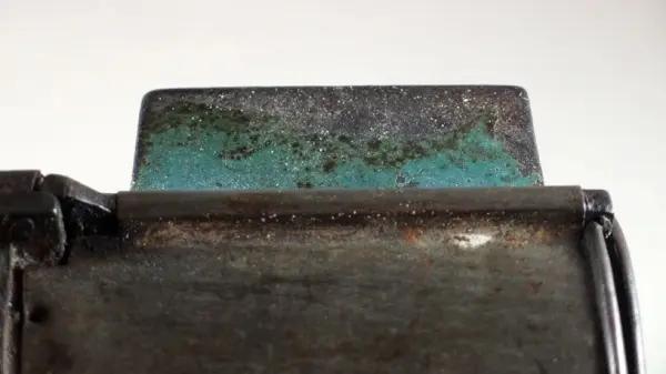 Ein metallisches Objekt mit Grünspan zeigt eine Reaktion, während Salmiakgeist zur Reinigung verwendet wird.