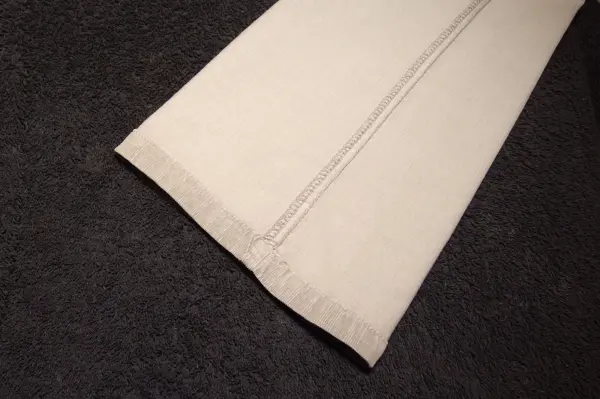 Ein Hosenbein mit klaren Bügelfalten liegt auf einem dunklen Hintergrund und zeigt die scharfen Materialien und Nähte.