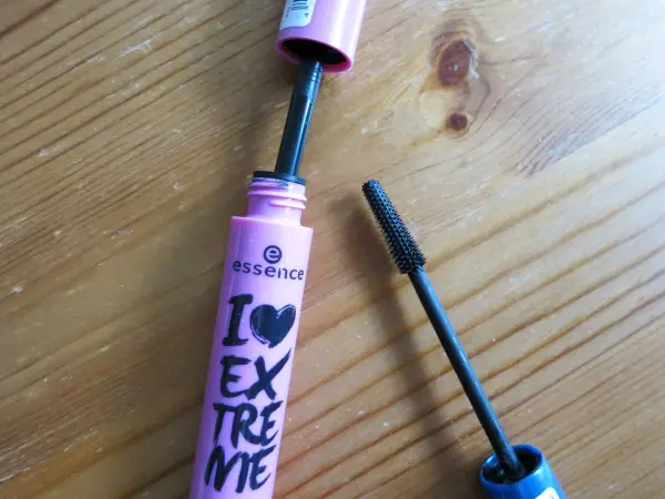 Eine geöffnete Wimperntusche liegt auf einem Holzuntergrund, während die Bürste bereit ist, verklumpte Wimpern zu bösen.