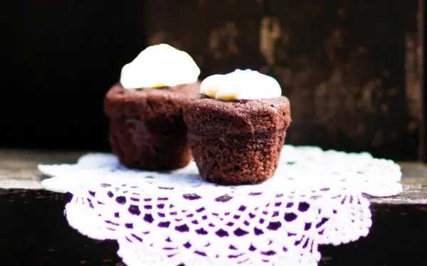 Zwei Schokomuffins mit flüssigem Kern stehen auf einer weißen Spitzenunterlage vor einem dunklen Hintergrund.