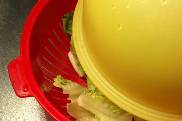 Ein gelber Salatspinner ist auf einem roten Sieb platziert, während frisch gewaschener Salat darin wartet, geschleudert zu werden.