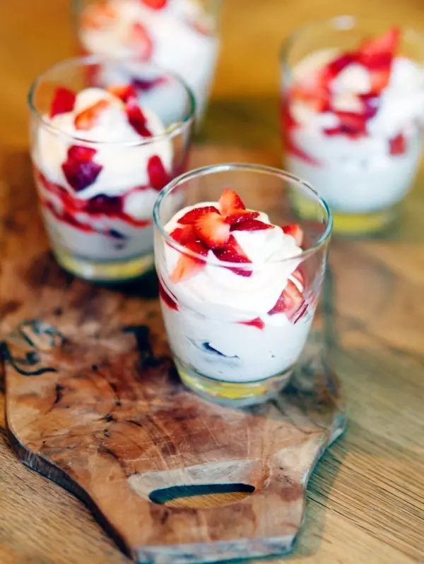 Gläser mit Beeren und Mascarponecreme stehen auf einem Holzbrett, umgeben von einer warmen, einladenden Küchenszene.