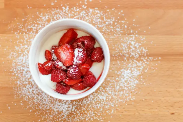 Eine Schüssel mit frischen Erdbeeren und Mascarpone ist auf einem Holztisch liebevoll angerichtet, mit Puderzucker bestäubt.