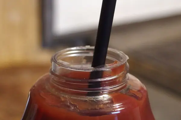 Ein Ketchupglas mit schwarzem Strohhalm steckt in der Flasche und steht auf einem Holzuntergrund in einer Küche.
