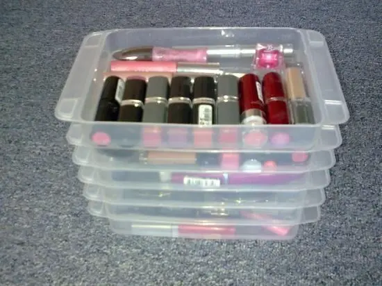Transparente Box mit ordentlich angeordneten Schminkartikeln, darunter Lippenstifte in verschiedenen Farben, auf einer Fläche.