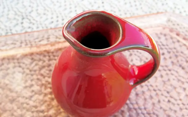 Eine rote Vase mit einem kleinen Riss steht auf einem hellen Untergrund und zeigt Anzeichen von möglicher Reparatur.