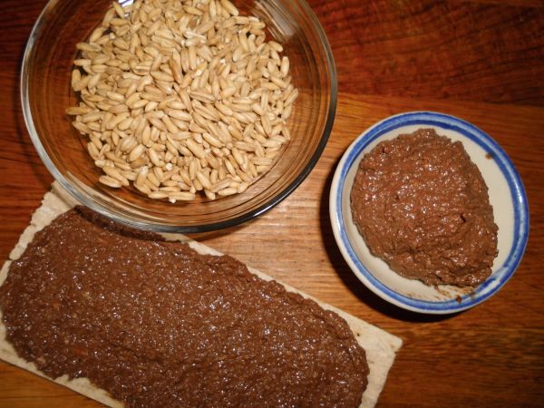Eine cremige Schoko-Hafer-Creme liegt auf einer Brotoberfläche, daneben sind Haferflocken und eine kleine Schüssel mit Creme.