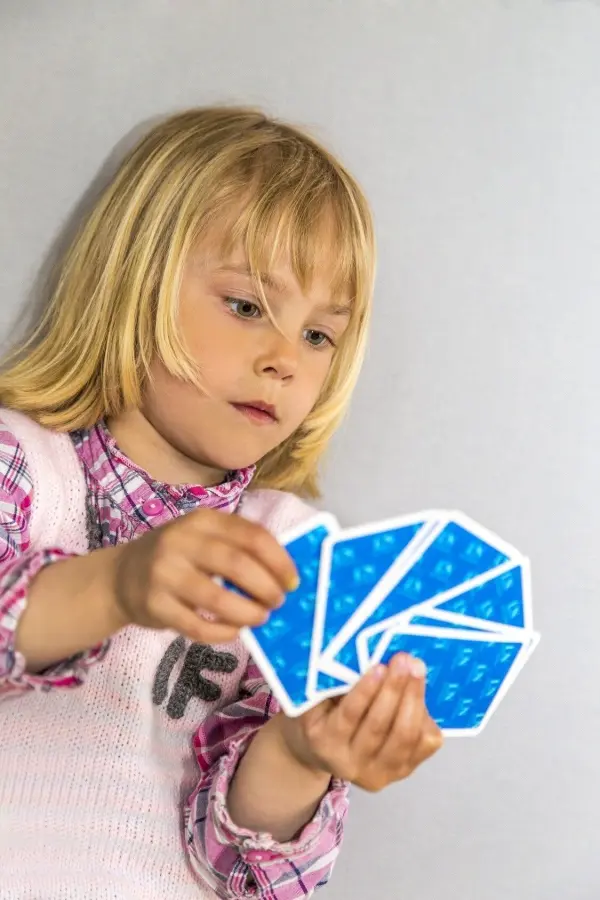 Kind hält blaue Spielkarten in der Hand, konzentriert in neutralem Hintergrund.