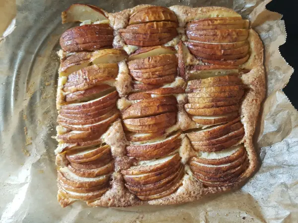 Ein köstlicher, goldbraun gebackener Apfelkuchen mit dünn geschnittenen Äpfeln, auf Backpapier in einer Auflaufform liesst.