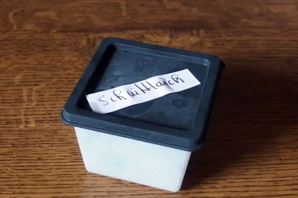 Eine Gefrierdose steht auf einem Holztisch und trägt ein handschriftliches Etikett zur Kennzeichnung des Inhalts.