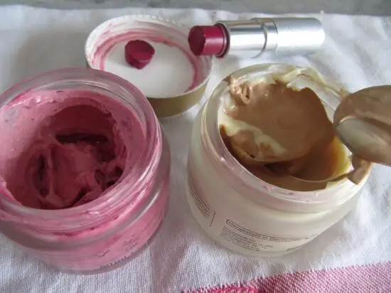 Zwei offene Töpfe mit getönter Tagescreme und Rouge, während ein Löffel in die Creme eingetaucht wird.