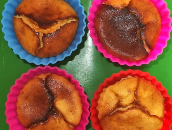 Käsekuchen in Förmchen zeigt vier kleine, gebräunte Küchlein in bunten Silikonformen auf einer grünen Unterlage.