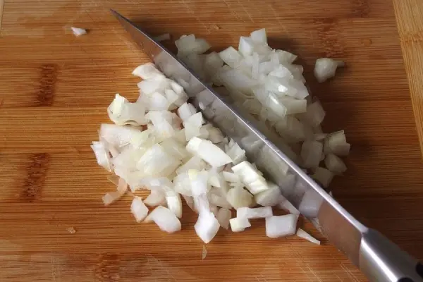Kleine, gewürfelte Zwiebeln liegen auf einem Holzbrett, während ein scharfes Messer sie zerteilt, um ein Gericht zuzubereiten.