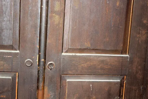Dunkle Türen aus Holz stehen nebeneinander, leicht geöffnet, und lassen schummriges Licht in den Raum strömen.