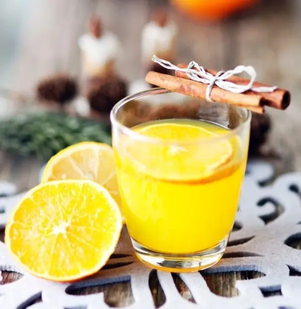 Ein warmes Glas O-Saft steht auf einem rustikalen Tisch, umgeben von frischen Zitronenscheiben und einer Zimtstange.