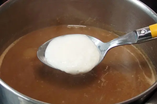 Ein Löffel Quark wird in eine kochende Brühe gegeben, um als kalorienarmer Soßenbinder zu wirken.