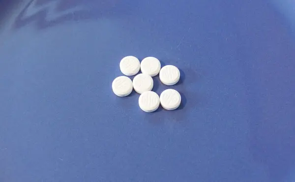 Sechs kleine weiße Tabletten liegen auf einem blauen Untergrund und deuten auf die Verwendung von Schüßler-Salzen gegen unreine Haut hin.