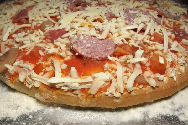 Eine Pizza mit Käse und Salami liegt auf einer bemehlten Fläche, bereit für das Backen, um knusprig zu werden.