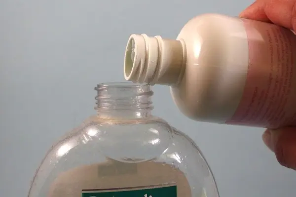 Eine Hand gießt Shampoo in einen leeren Flüssigseifen-Behälter, bevor er für die Dusche verwendet wird.