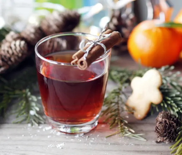 Ein Glas Glühwein-Sangria steht auf einem Tisch, umgeben von Tannenzweigen, einer Orange und einem Plätzchen.