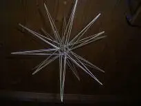 Ein dreidimensionaler Deko-Stern aus Gräsern hängt vor einer Holzwand, spitz zulaufend und geometrisch ansprechend.