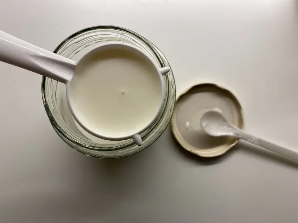Ein Glas mit selbstgemachtem Kefir wird mit einem Löffel abgehoben, um die cremige Konsistenz zu zeigen.