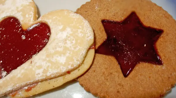 Zwei liebevoll dekorierte Plätzchen liegen auf einem Teller, eines mit Herzform und das andere sternförmig, gefüllt mit Marmelade.
