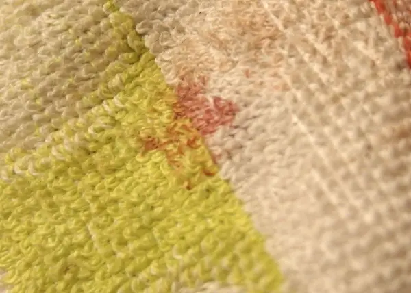 Ein Textil zeigt einen kleinen Blutfleck, der auf einer bunten, strukturierten Oberfläche sichtbar ist.