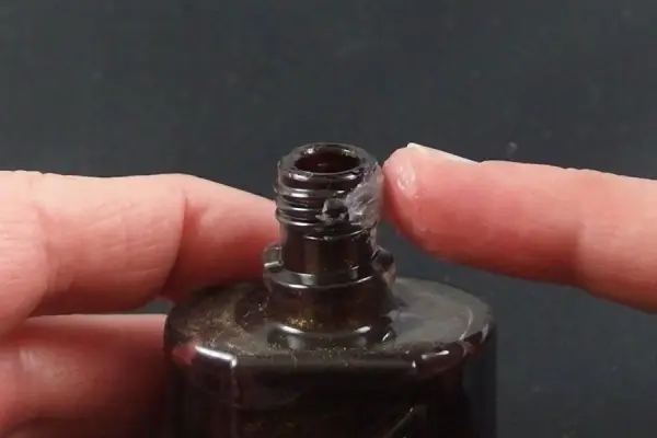 Ein Nagellackfläschchen wird mit einem Finger berührt, um es zu öffnen, während es auf einem dunklen Untergrund steht.