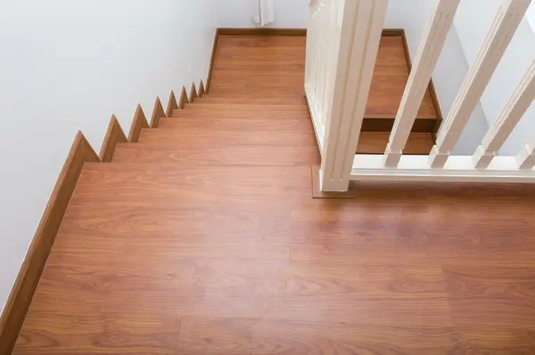 Laminatboden glänzt streifenfrei auf Treppe neben weißem Geländer in modernem Treppenhaus mit heller Wand.