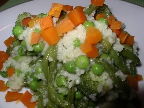 Couscous mit grünem Gemüse und Karottenwürfeln wird appetitlich auf einem Teller serviert, umgeben von frischer Kräutersauce.