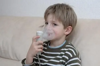 Ein Kind benutzt ein Inhalationsgerät mit Atemmaske und hält den Griff auf einem Sofa sitzend in einem gemütlichen Zimmer.