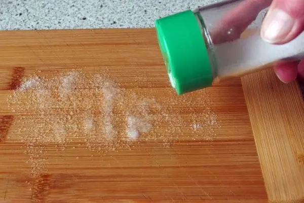 Ein Hand registriert ein Schneidbrett aus Holz, während Salz darüber gestreut wird, um Gerüche zu neutralisieren.