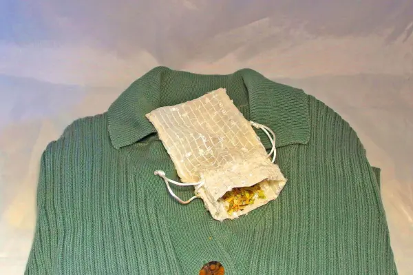 Ein grüner Pullover liegt flach mit einem kleinen Säckchen aus Naturmaterial, das duftende Zutaten enthält.