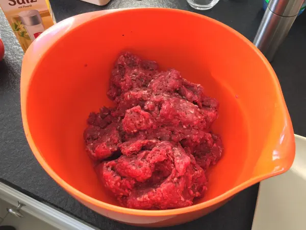 In einer orangenen Schüssel liegt rohes Hackfleisch, bereit für die Zubereitung des Original American Cheeseburgers in einer Küche.