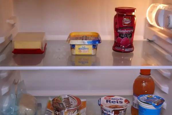Ein Kühlschrank steht geöffnet und zeigt verschiedene Lebensmittel wie Butter, Marmelade und Getränke auf den Regalen.