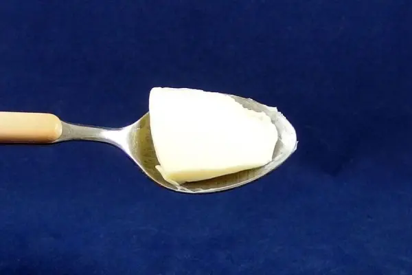 Ein Löffel mit Butter steht im Vordergrund und zeigt, wie das Lebensmittel zur Linderung von Halsschmerzen eingesetzt werden kann.
