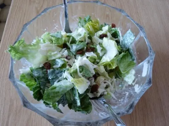 Ein bunter Sauerkrautsalat mit Mini-Romana wird in einer gläsernen Schüssel serviert, umgeben von einem hellen Holzuntergrund.