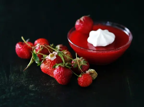 Eine Schüssel Erdbeer-Kaltschale mit Sahne steht auf einem dunklen Untergrund, umgeben von frischen Erdbeeren.