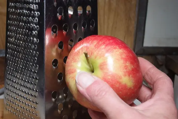 Ein roter Apfel wird mit einer Hand an einer Käsereibe gerieben, um gesunde Nahrungsmittel bei Durchfall zuzubereiten.