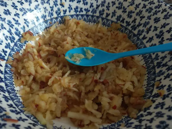 Ein bunter Schüssel mit geriebenem Apfel, in dem ein blauer Löffel ruht, zeigt eine geeignete Ernährung bei Durchfall.